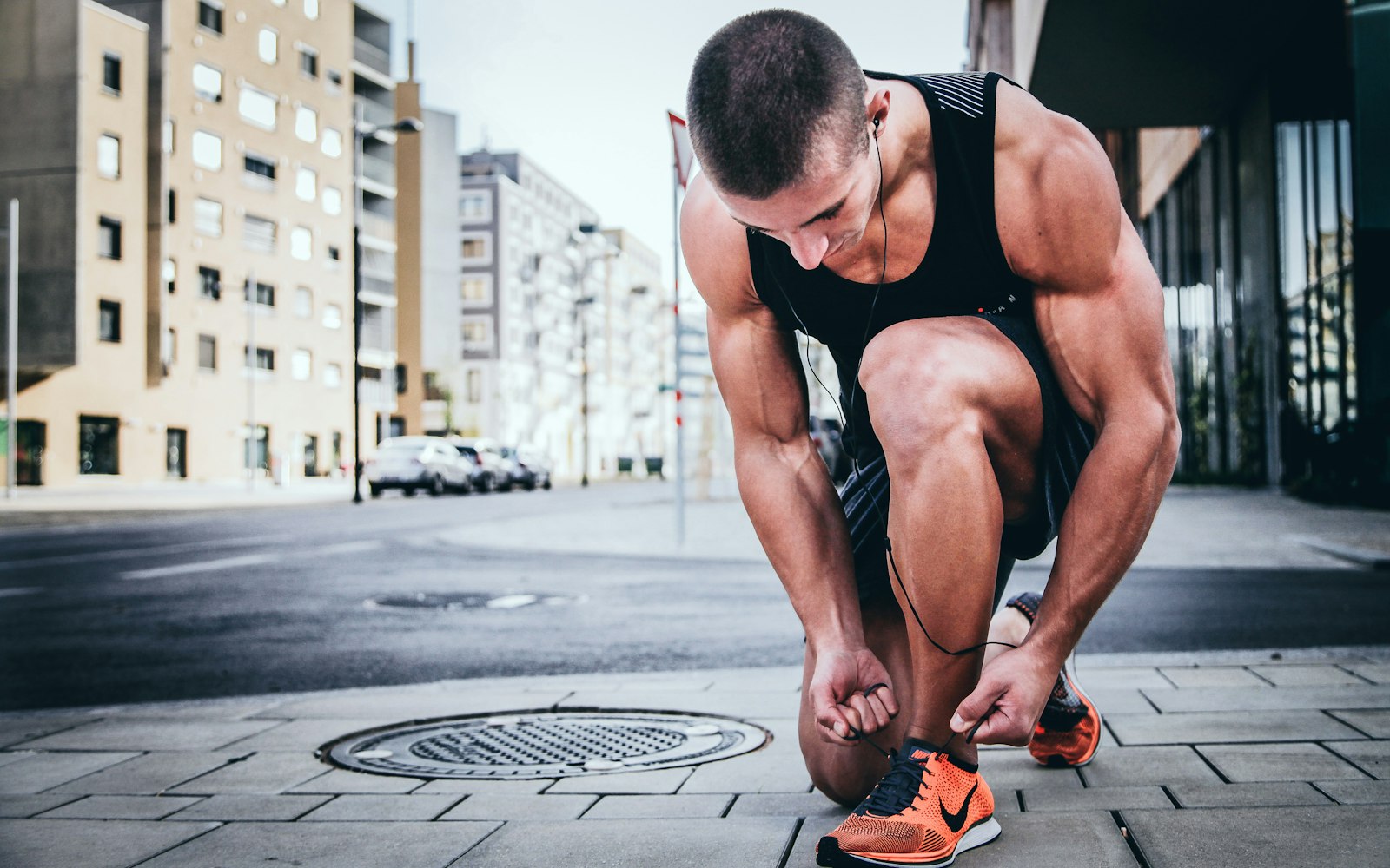 A runner kneeling on the pavement to tie the laces of his running shoes before a run