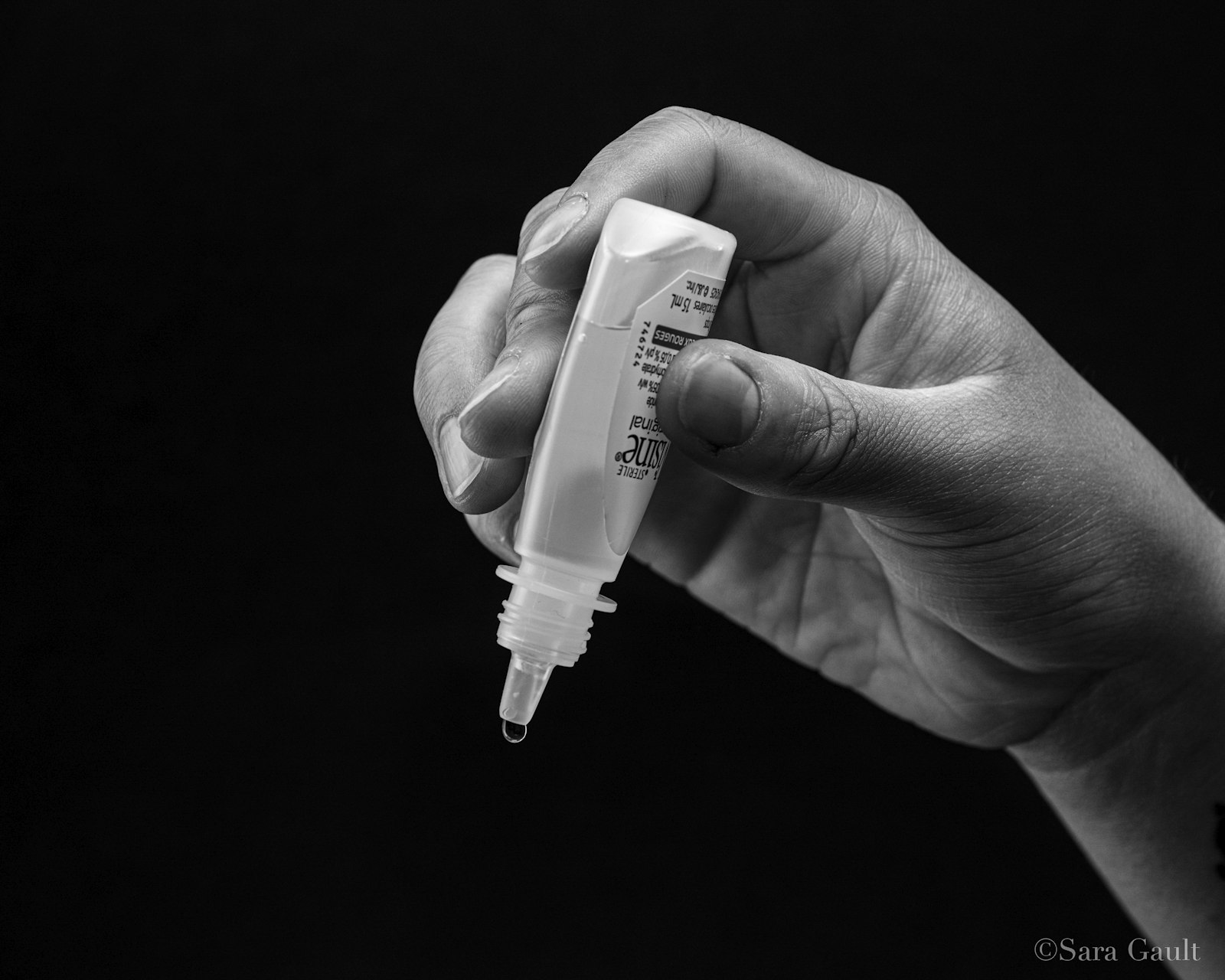 Black and white photo of a hand holding a small eye drop bottle