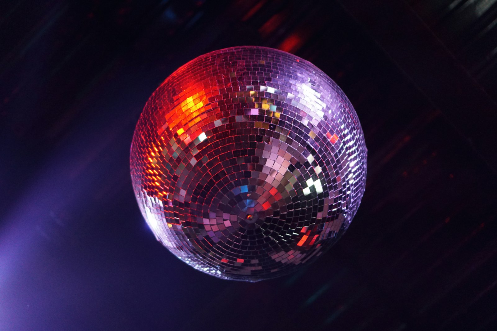 A mirror ball hanging in a dark room lit in deep purple, evoking a school prom night