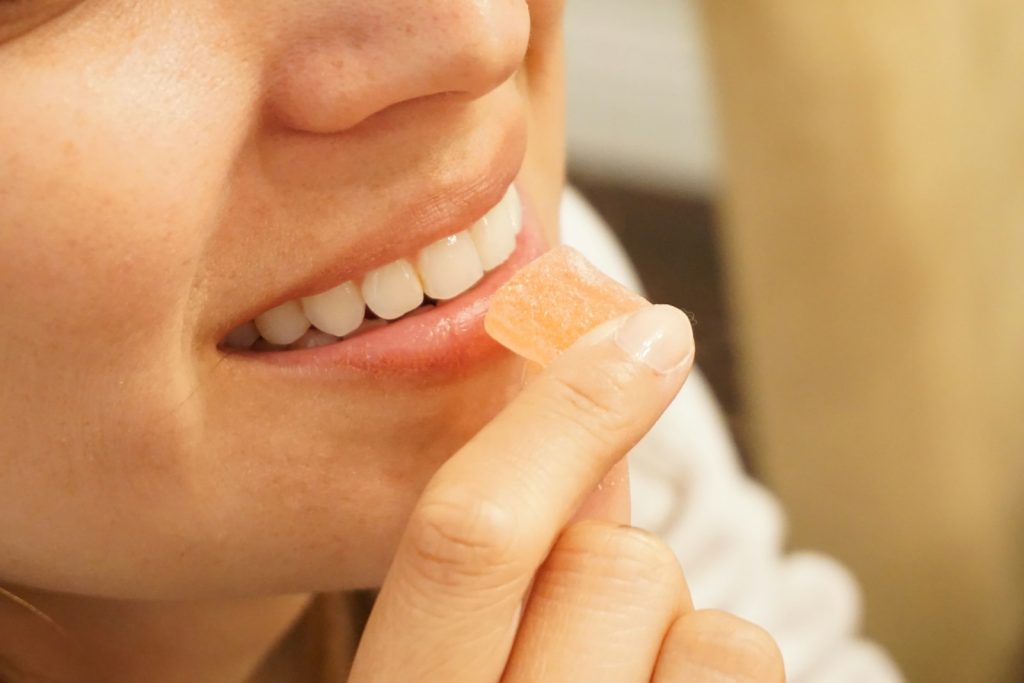 Close-up of a hand holding an orange and white gummy against a soft neutral background