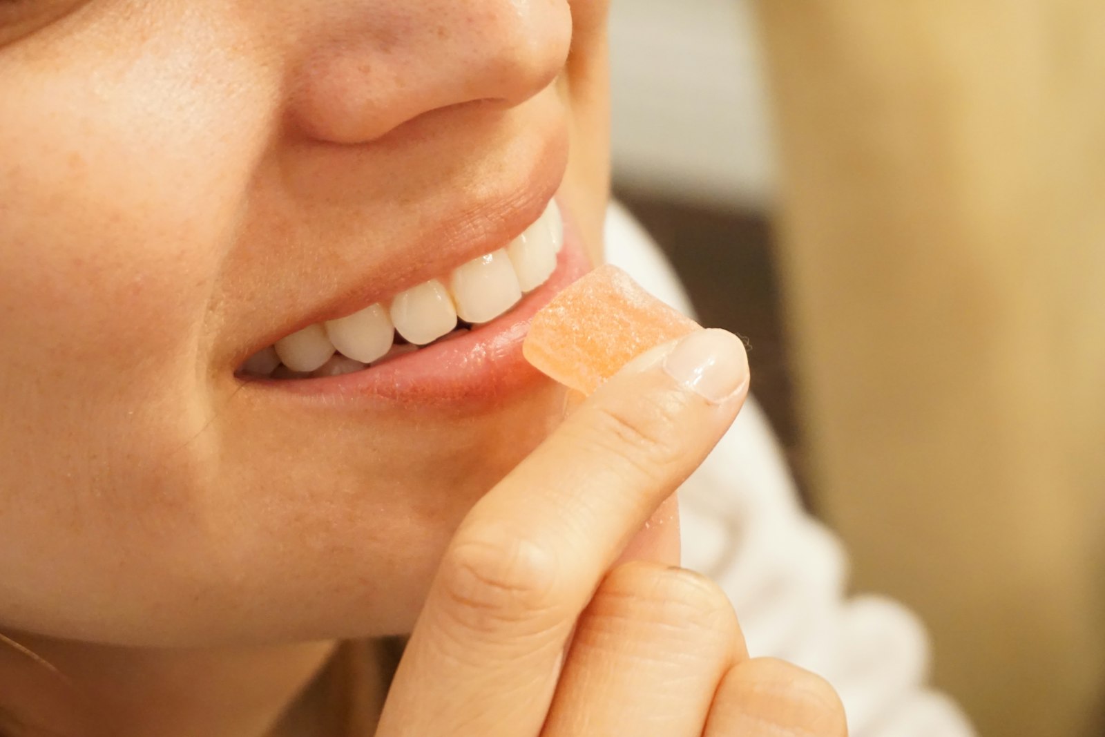 Close-up of a hand holding an orange and white gummy against a soft neutral background