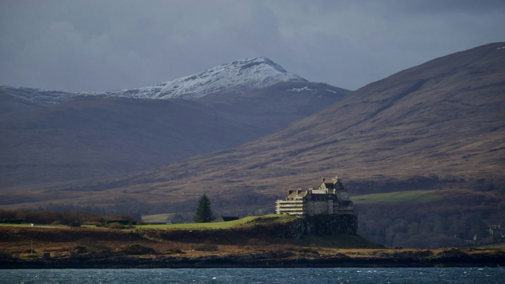 Scottish castle on a hill above the water with mountains under a moody sky