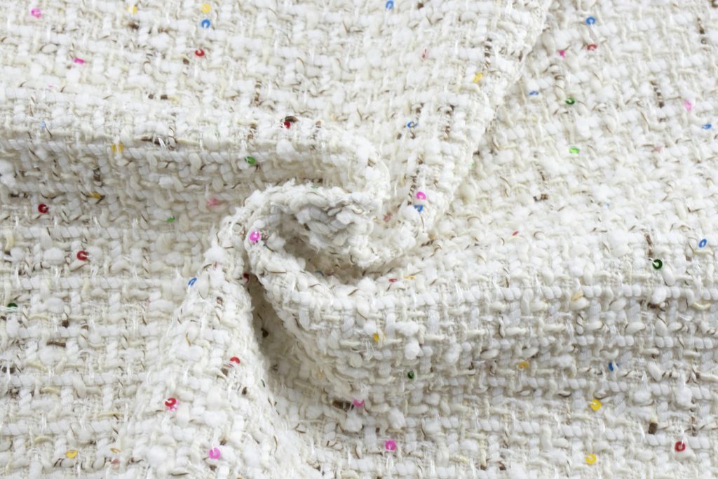Close-up of a pale bouclé tweed fabric woven with colorful sequins