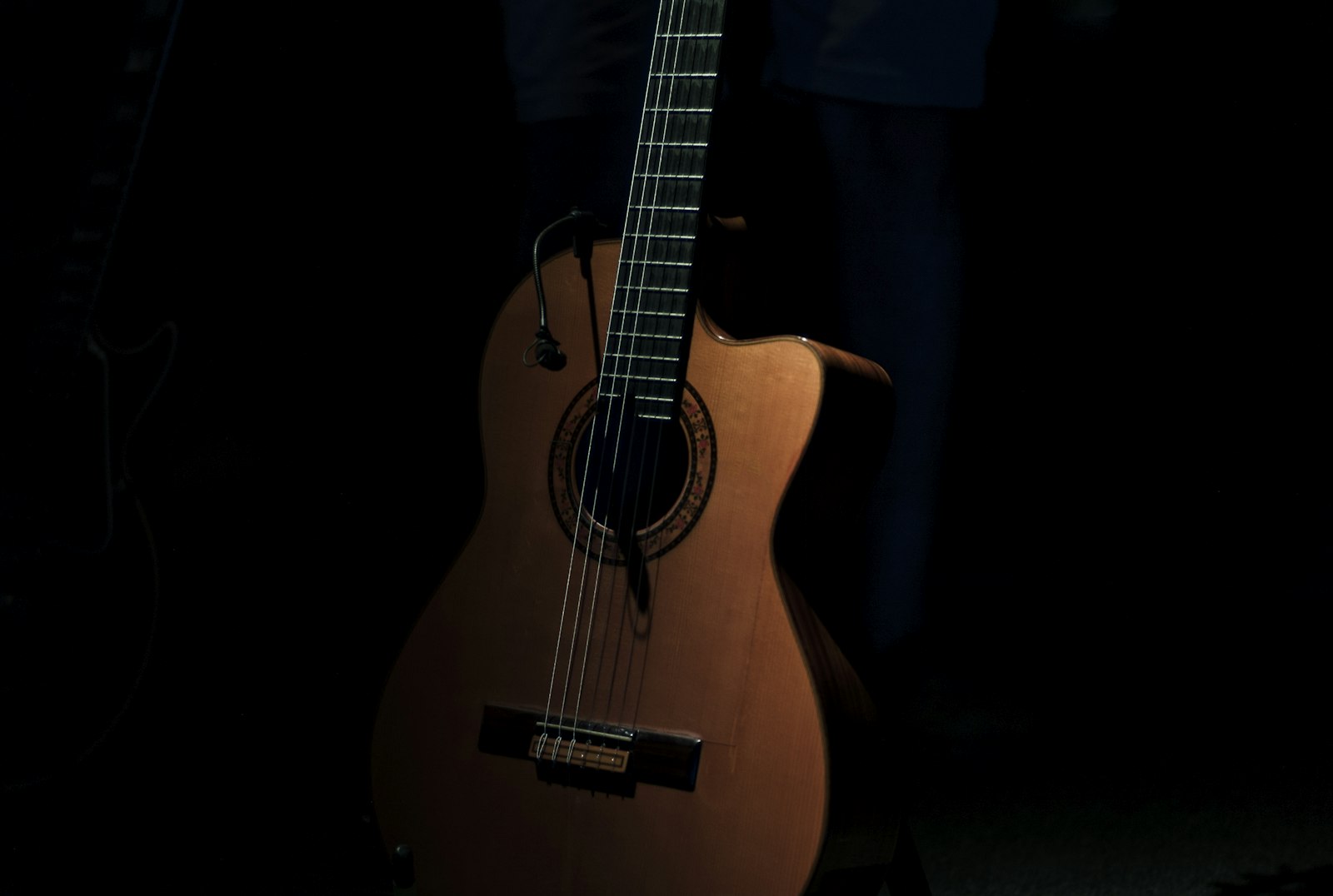 Close-up of a brown cutaway acoustic guitar in warm low light against a dark background