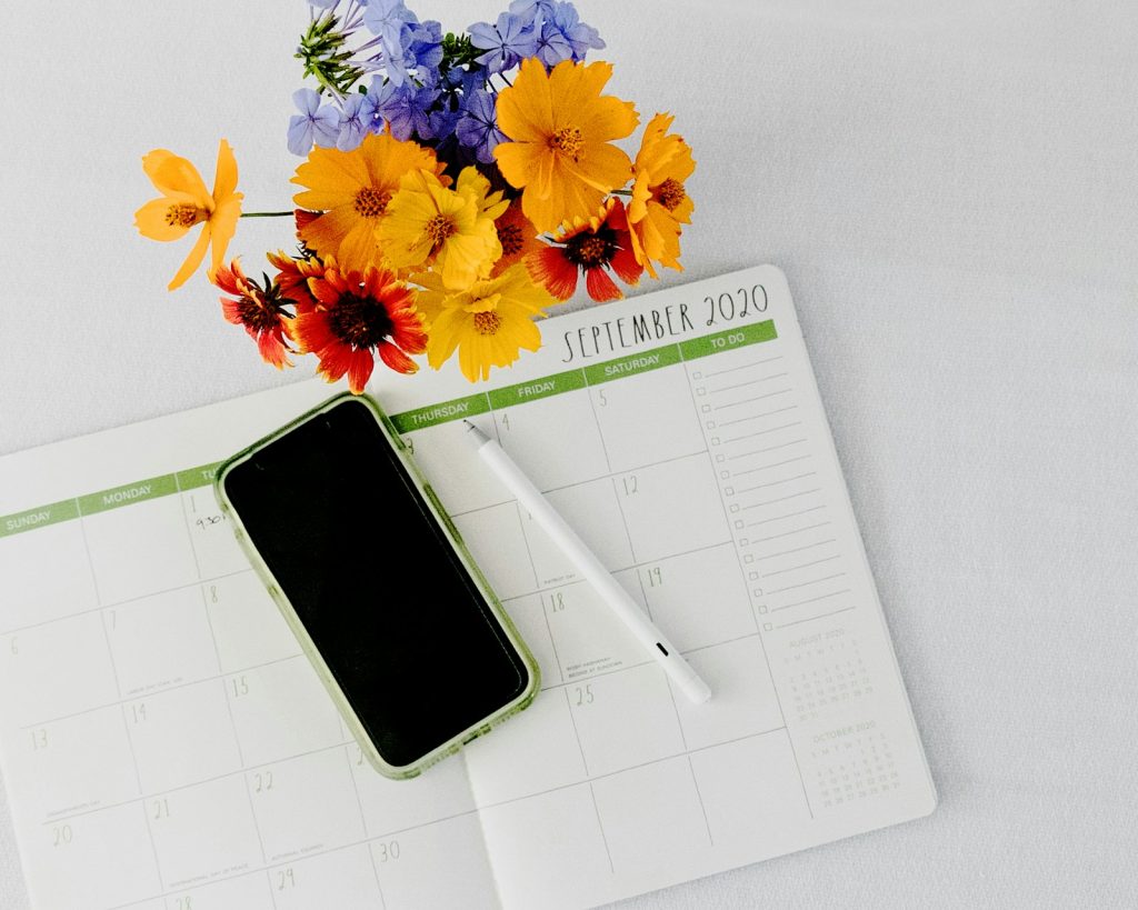 Smartphone lying on a paper monthly planner next to pens, symbolising cycle tracking and digital calendars