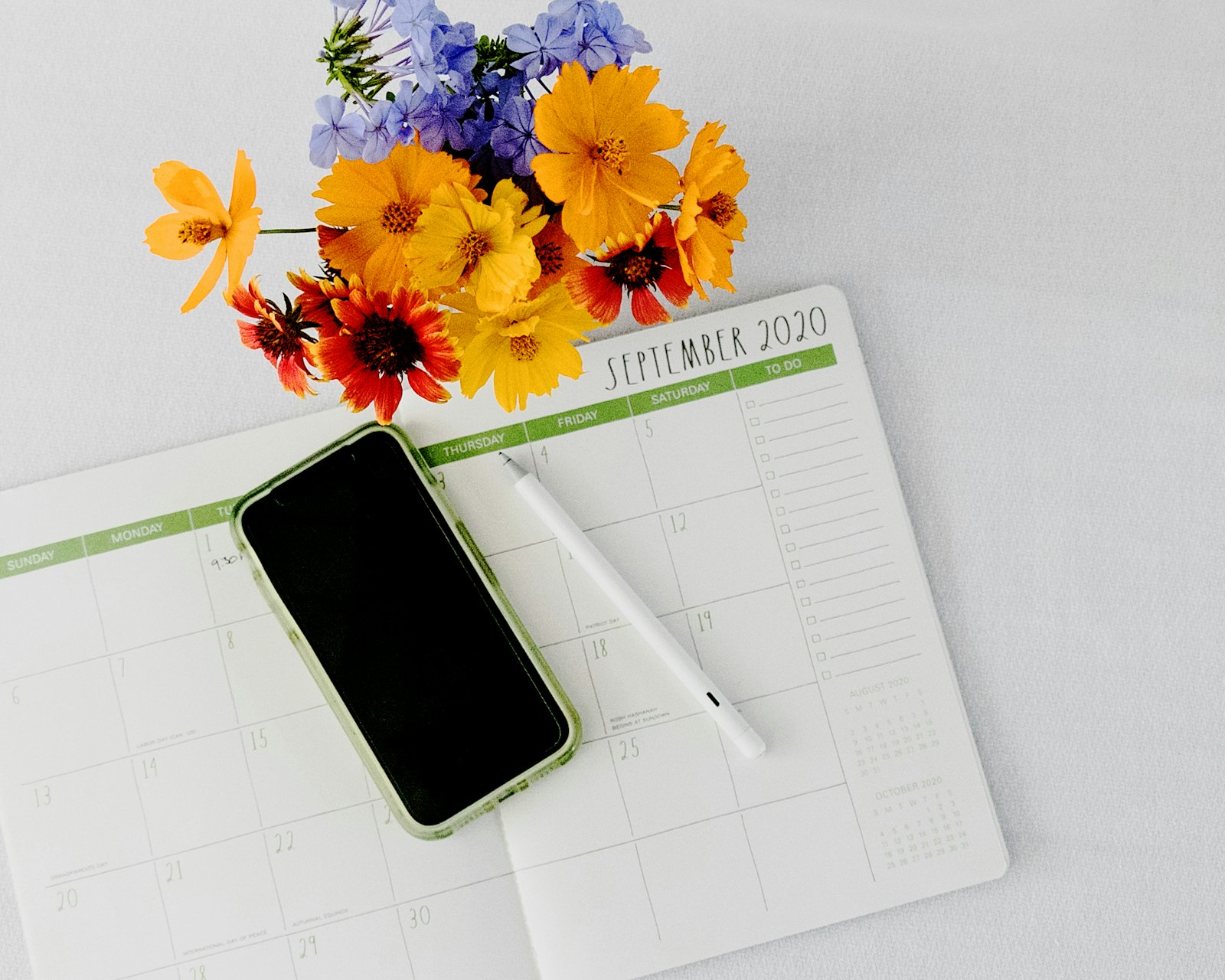 Smartphone lying on a paper monthly planner next to pens, symbolising cycle tracking and digital calendars