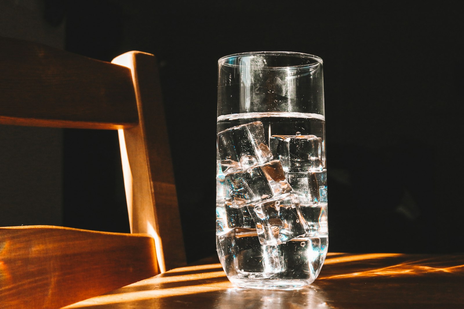 A clear drinking glass of water on a dark wooden table, illustrating the choice between water and diet drinks