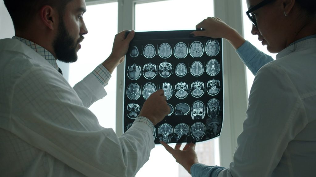 Two doctors in white coats discussing brain MRI images on a screen in a hospital office