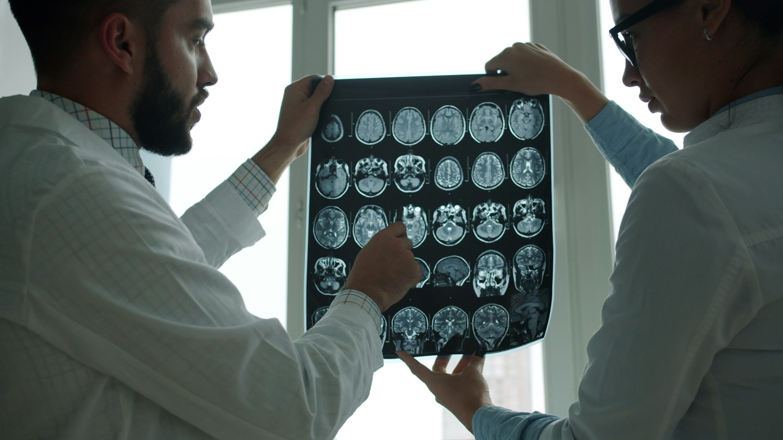 Two doctors in white coats discussing brain MRI images on a screen in a hospital office
