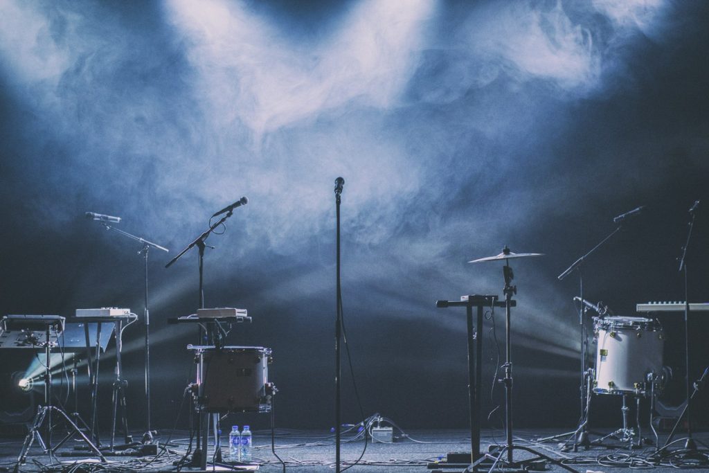 Musical instruments and microphones on a dark concert stage with blue spotlights and thick haze