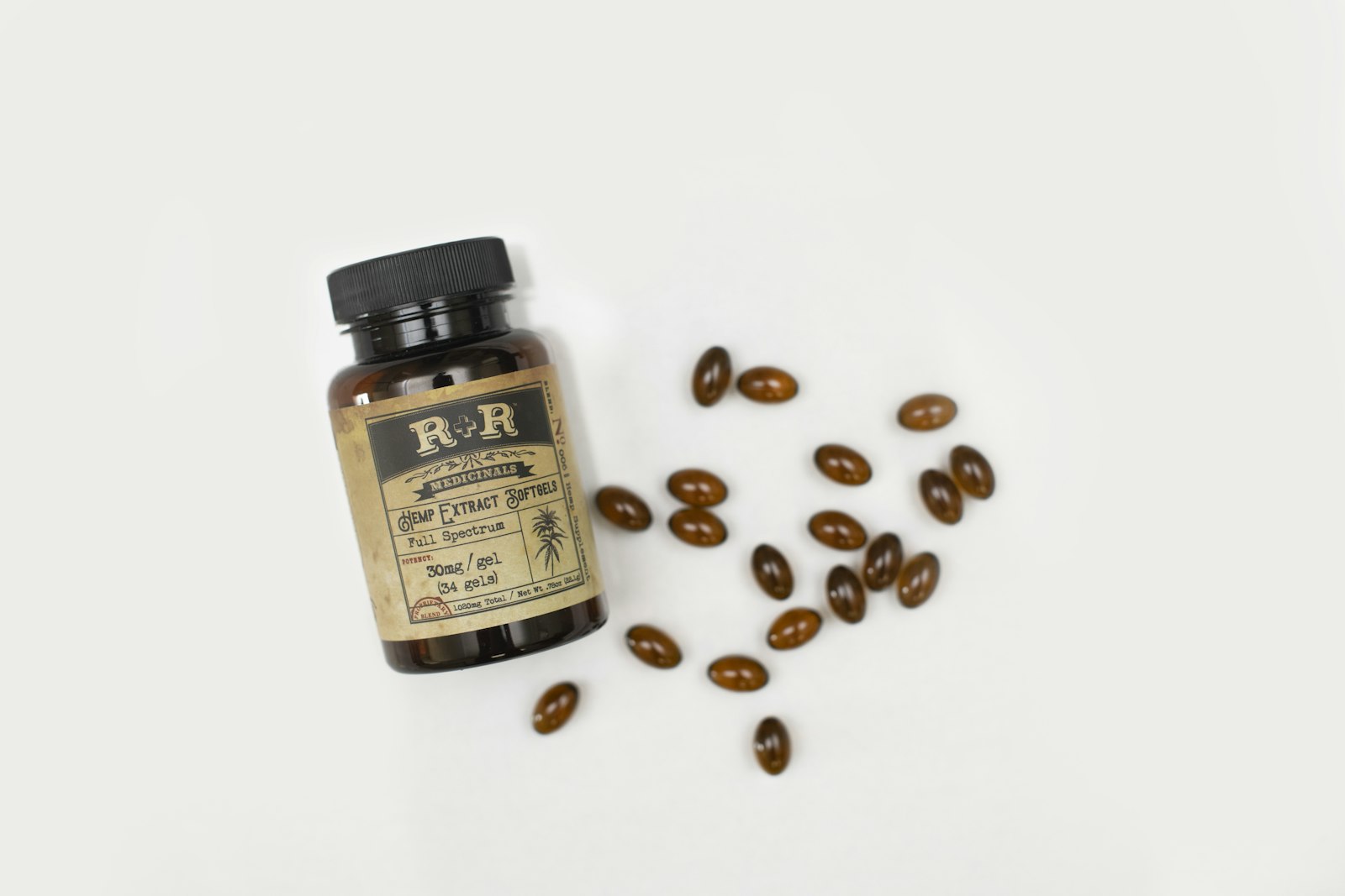 Brown supplement capsules spilling from an amber bottle on a white surface