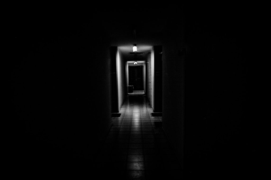A dark hallway with a single light glowing at the far end, evoking the mood of a horror film