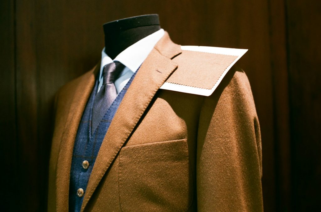 A dark tailored suit jacket with shirt and tie displayed on a tailor's mannequin