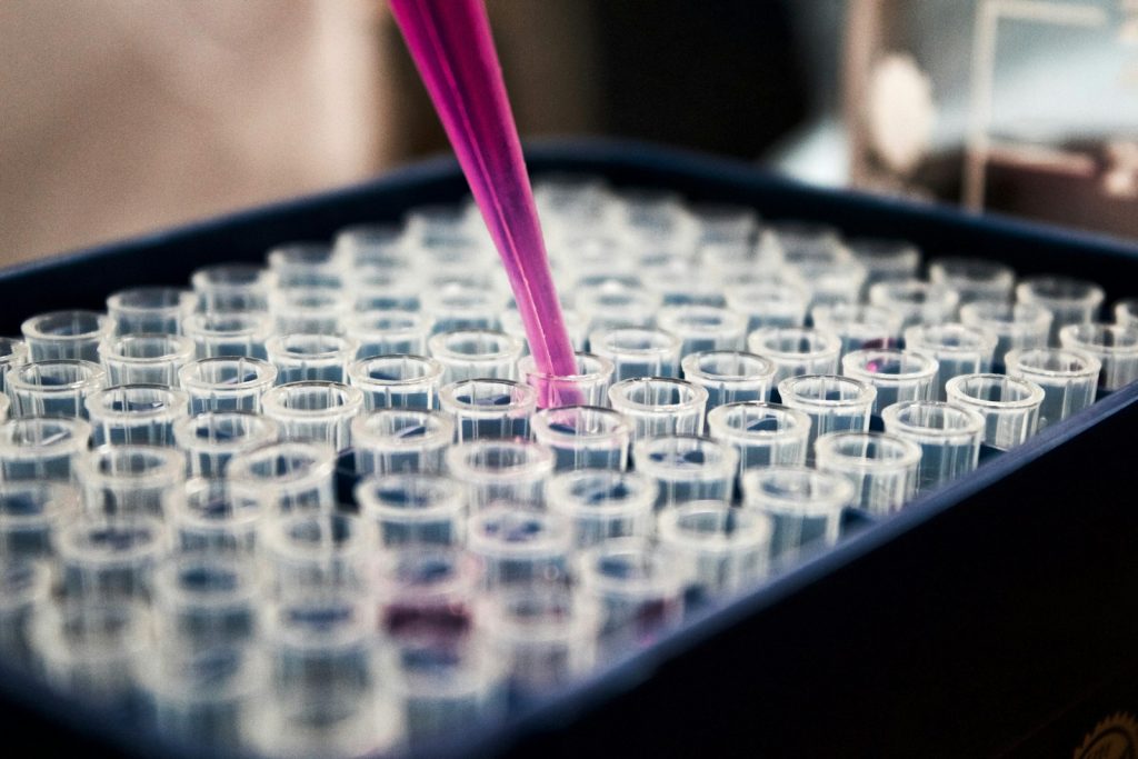 A pipette dispensing purple liquid into a row of test tubes in a research laboratory