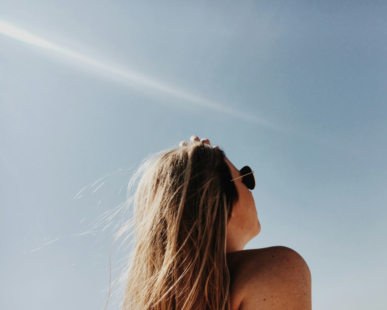 Frau mit goldgerahmter Pilotensonnenbrille im hellen Sonnenlicht – Symbolbild für UV-Schutz und Hautgesundheit