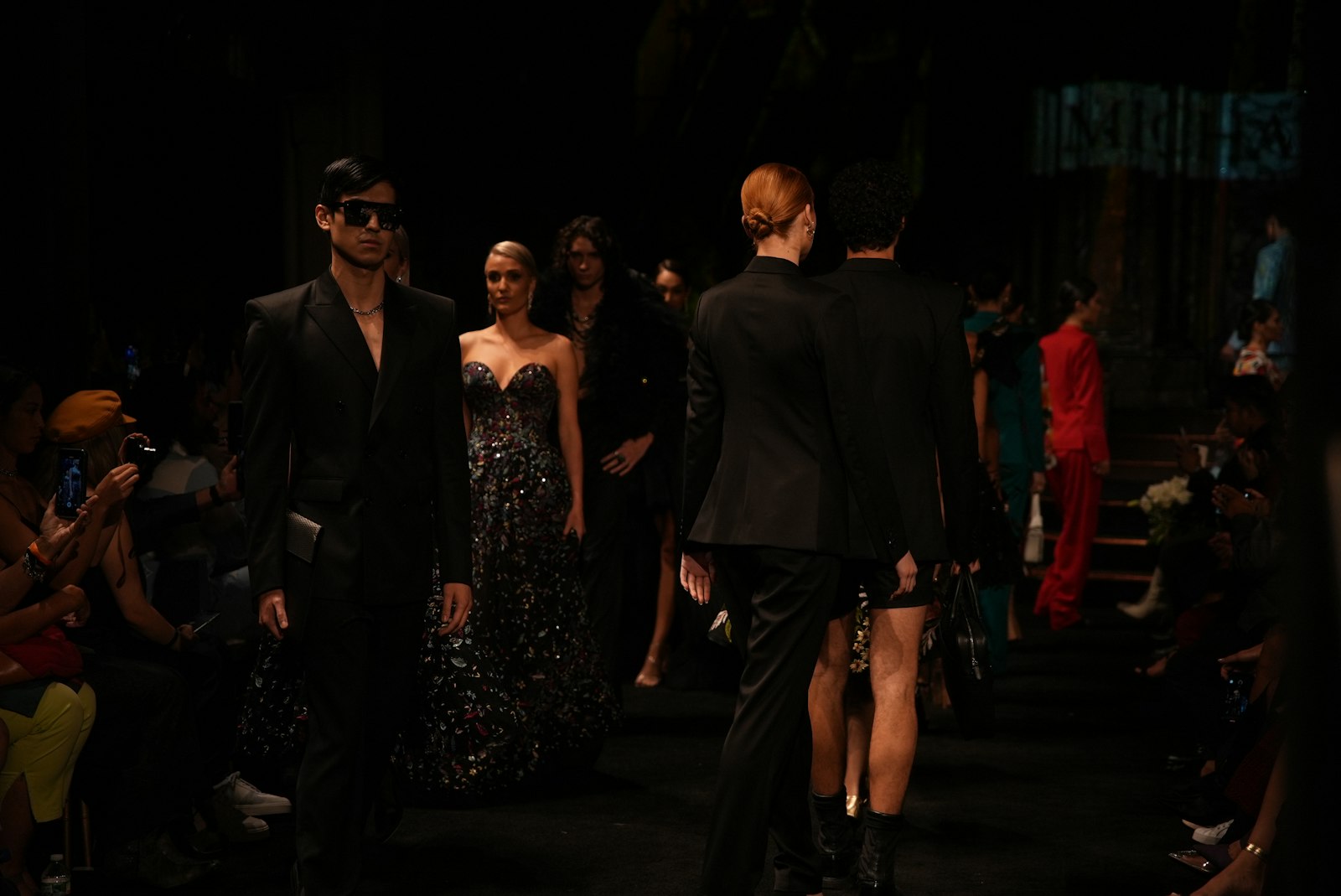 Fashion models walking down a dimly lit runway in dramatic red and black light