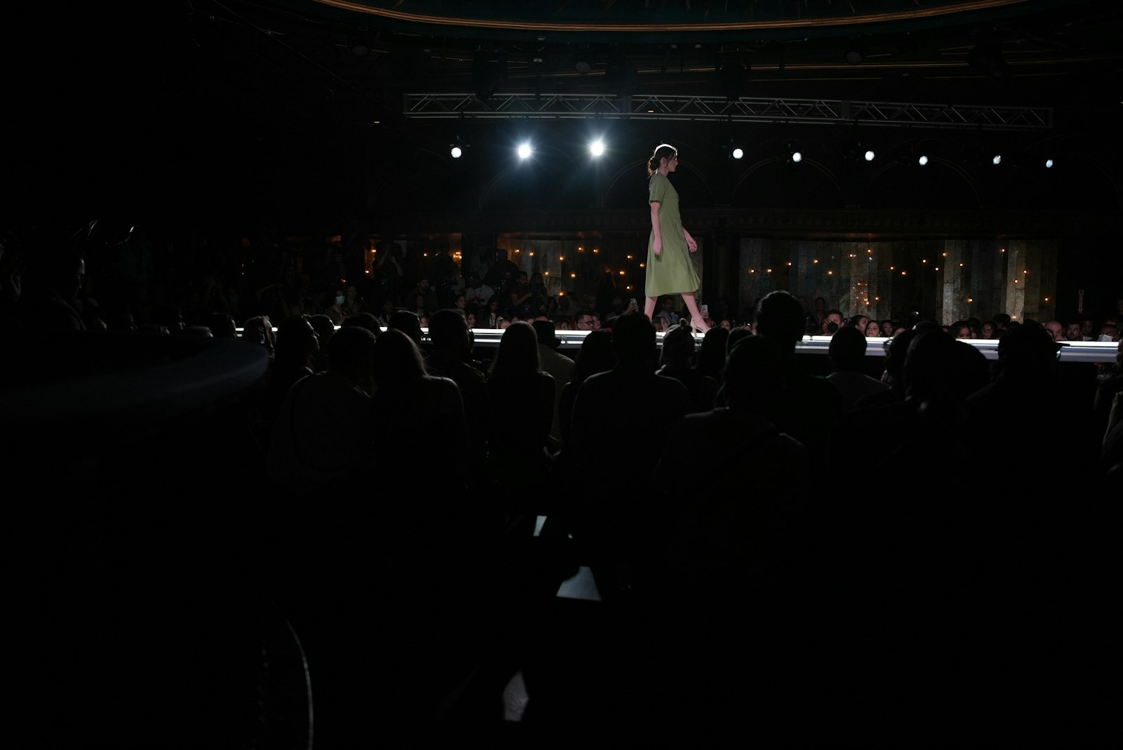 A fashion model walks a dark runway under bright spotlights, symbolising a minimalist designer show