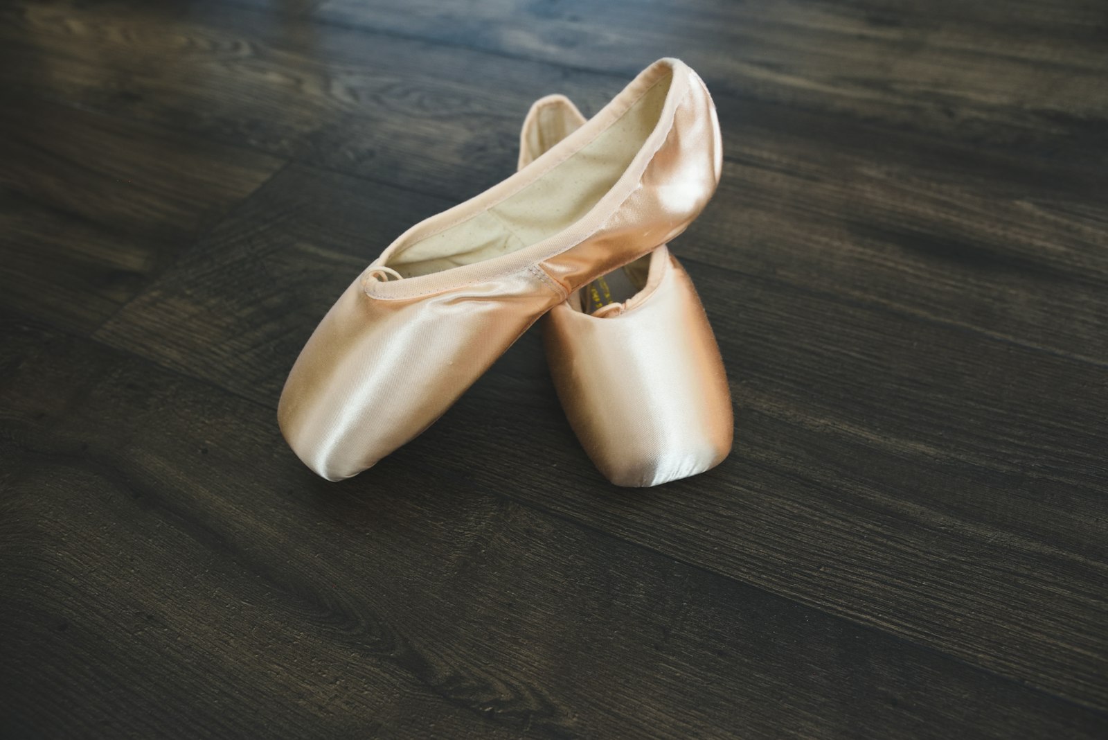 A pair of gold ballet flats standing on a dark wooden floor