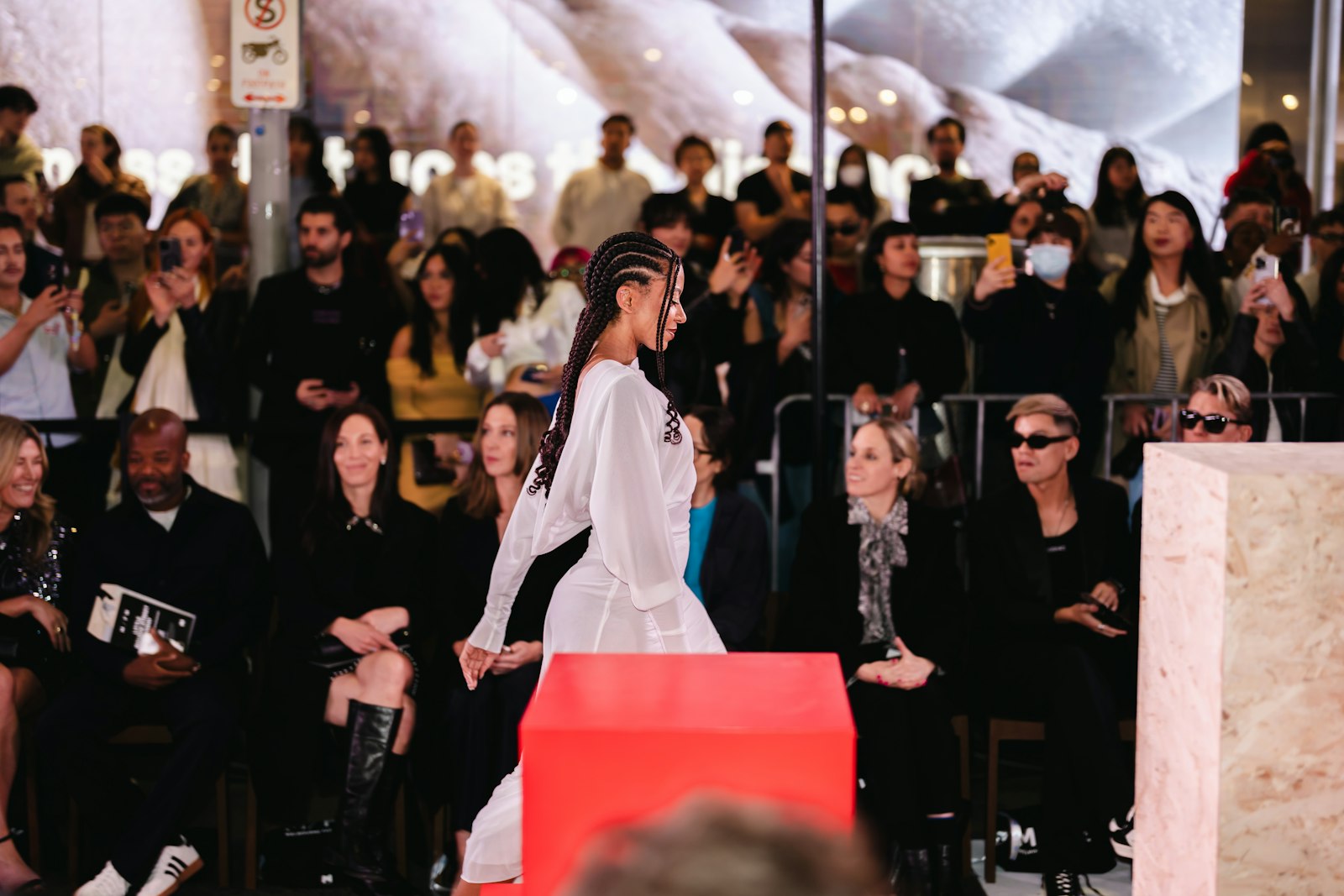 A model walks down a dimly lit fashion runway while the seated audience watches from both sides