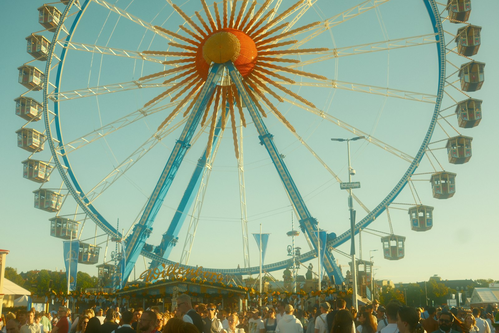Riesenrad über einer Menschenmenge auf einem Volksfest an einem sonnigen Tag – Symbolbild