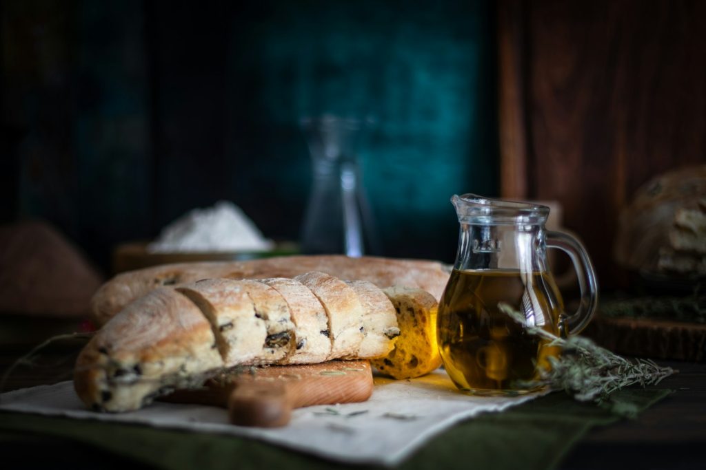 Slices of rustic bread with a dish of olive oil and fresh herbs on a dark table