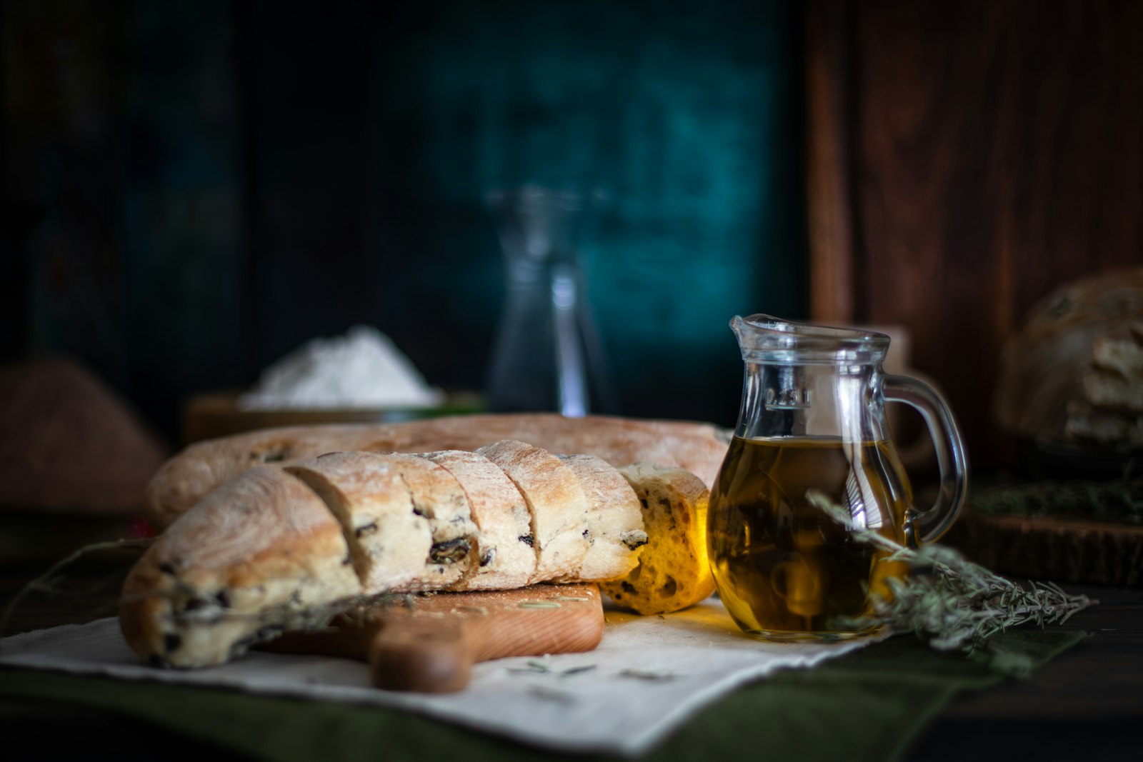 Slices of rustic bread with a dish of olive oil and fresh herbs on a dark table