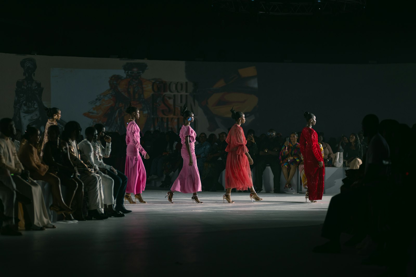 Models walking down a dark runway in a row during a fashion show