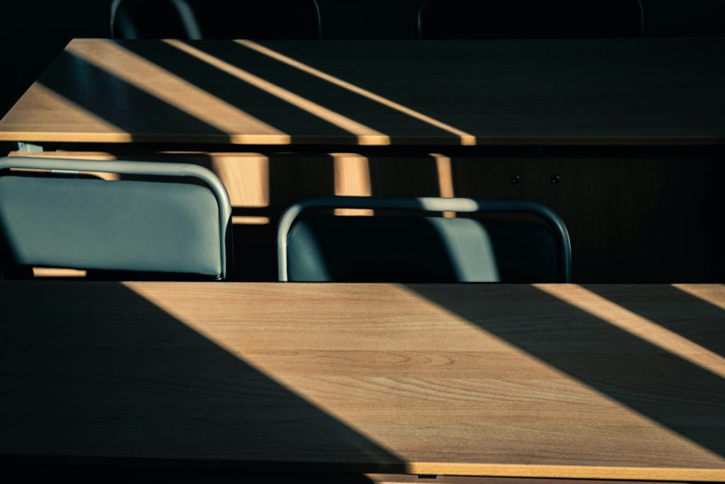 Sunlight falling through window blinds onto rows of empty wooden classroom desks