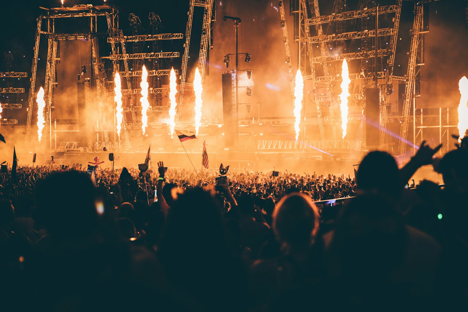 A large concert crowd watching flames and stage lights burst above a live performance at night