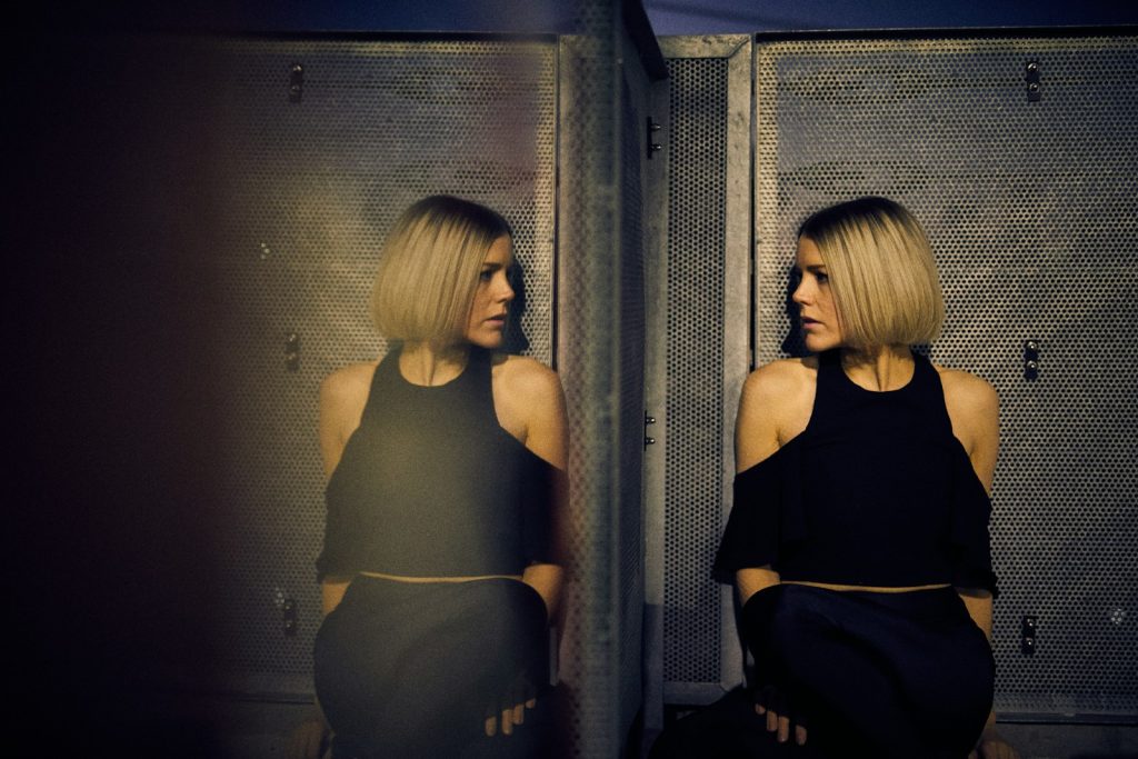 Moody dark portrait of a woman leaning against a wall beside a mirror, symbolising the mirrored runway mood of Tom Ford Spring 2027