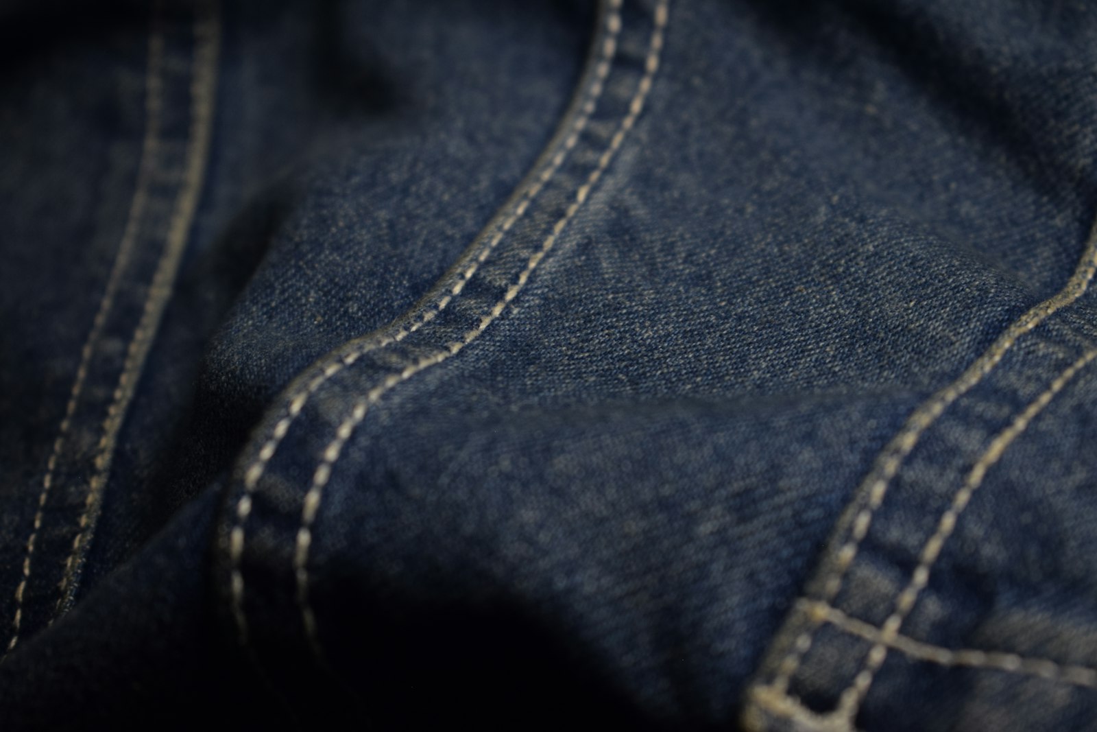 Close-up of dark blue denim fabric with thick white contrast stitching