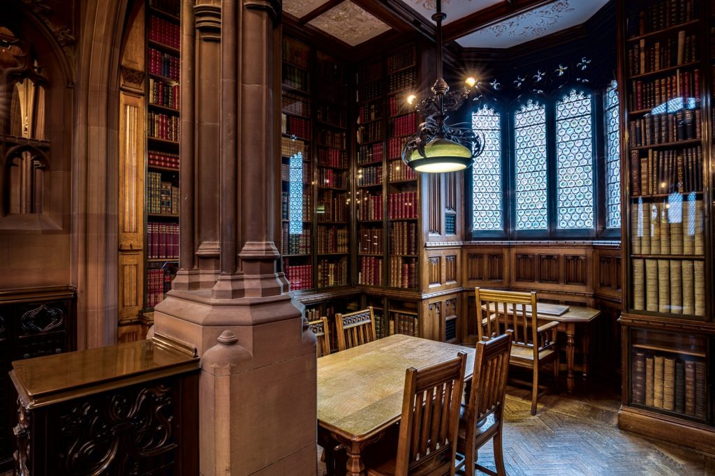 Ornate historic library reading room with long wooden tables, chairs and tall bookshelves