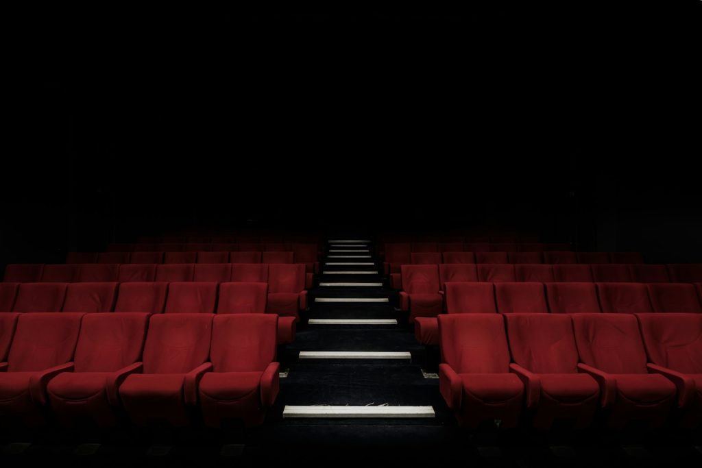 Rows of red velvet cinema seats in a dark movie theater