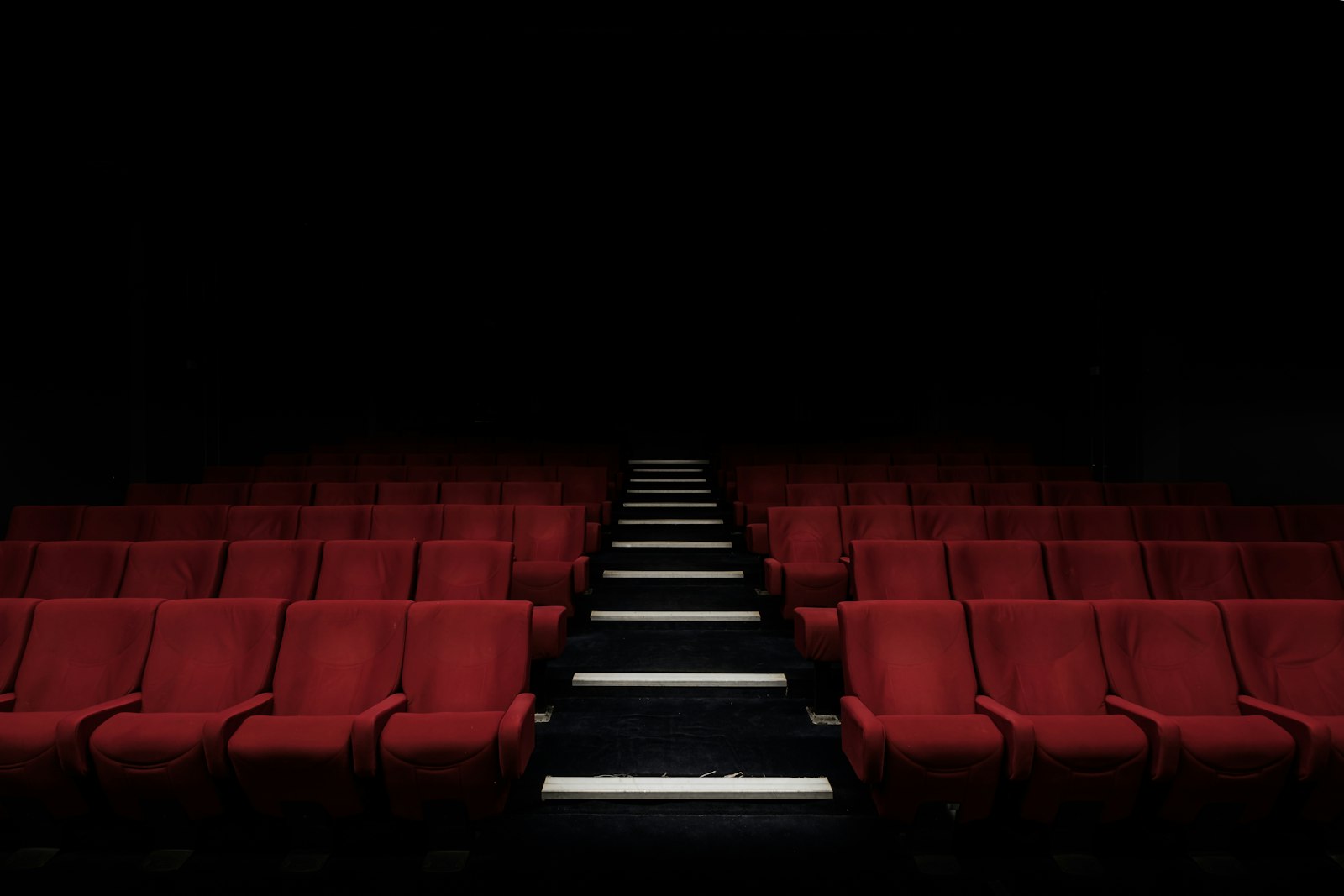 Rows of red velvet cinema seats in a dark movie theater