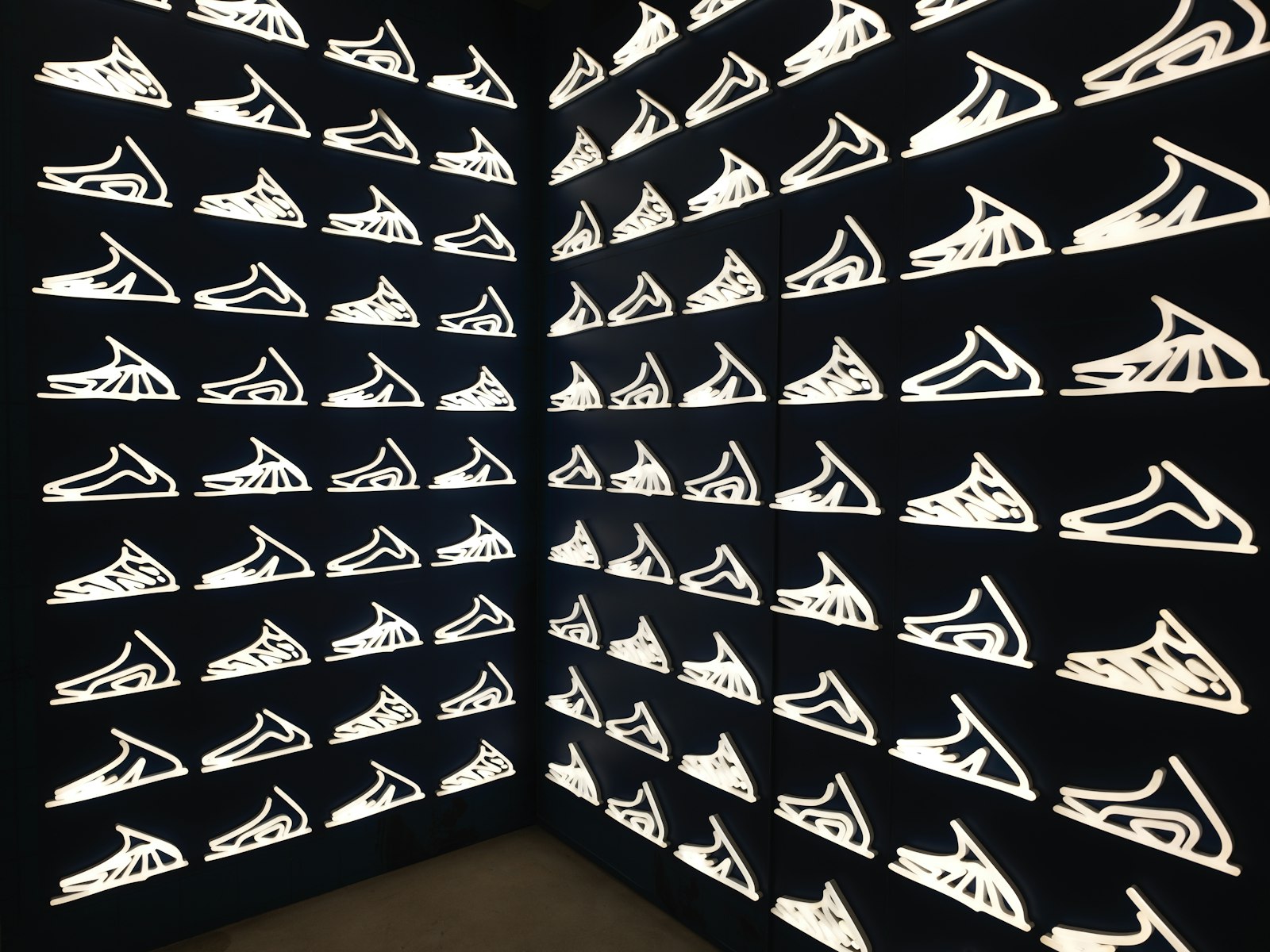 Rows of white sneakers displayed on a black wall like an art installation