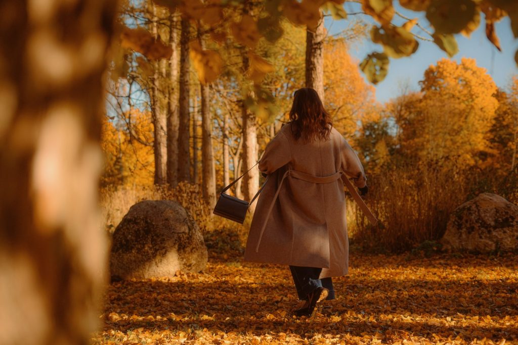 A woman walking along a path through an autumn forest with colorful leaves