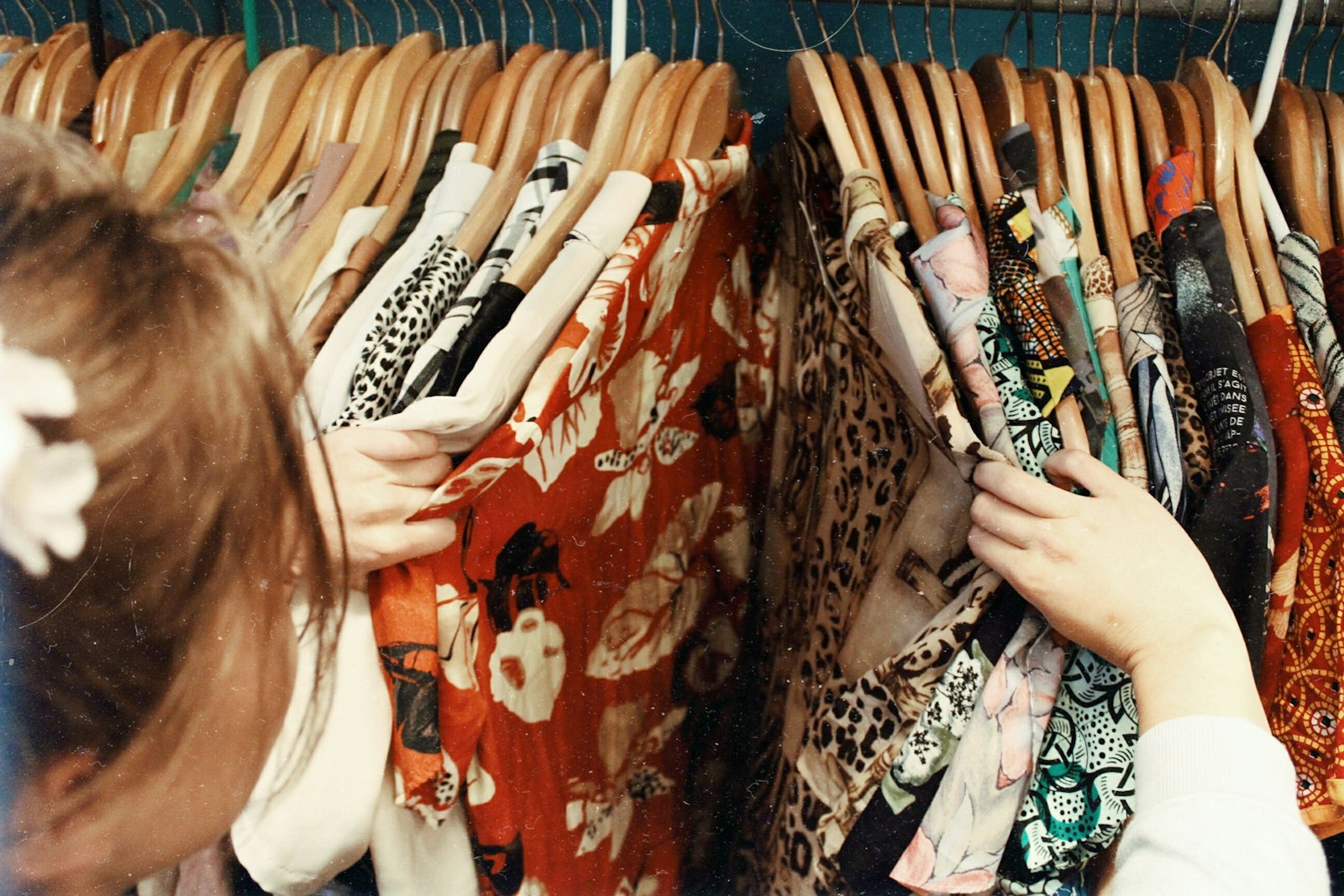 Hand browsing a rack of vintage patterned clothes on wooden hangers