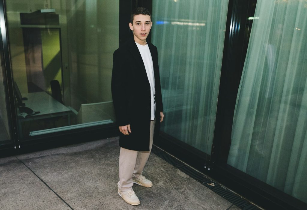Woman in a black blazer standing beside a glass wall, a symbol of minimal black tailoring